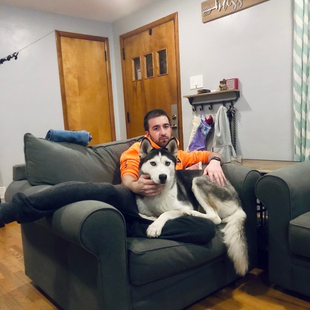 Guy sitting on couch with black and white husky
