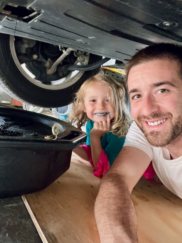 Father and young daughter changing the oil in car