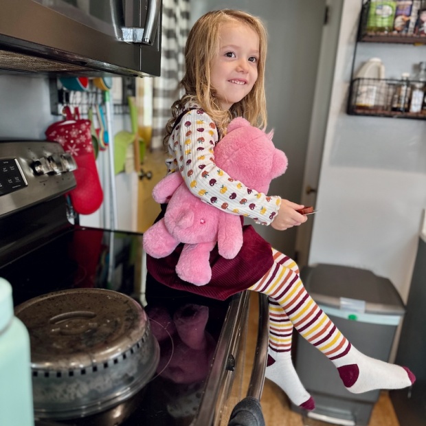 Girl sitting on stove holding pink Care Bear